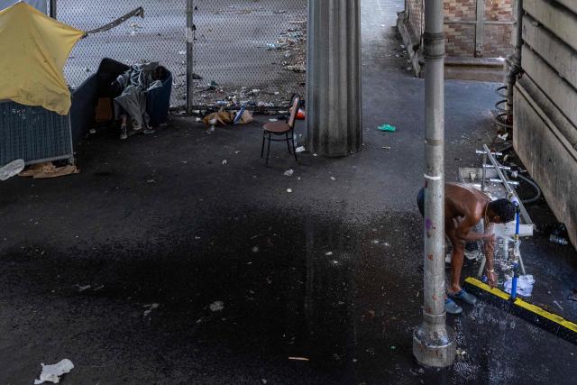 A homeless man washes off at a makeshift camp set up beneath the elevated Stalingrad metro station in Paris on July 3, 2026. (Photo by JOEL SAGET / AFP)