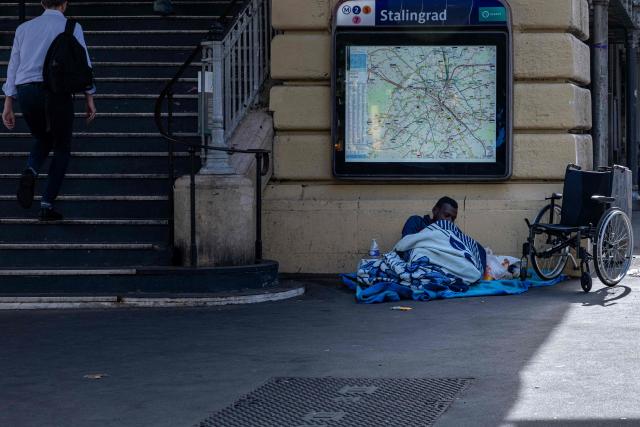 A homeless man lies on a makeshift bed at the entrance of the elevated Stalingrad metro station in Paris on July 3, 2026. (Photo by JOEL SAGET / AFP)