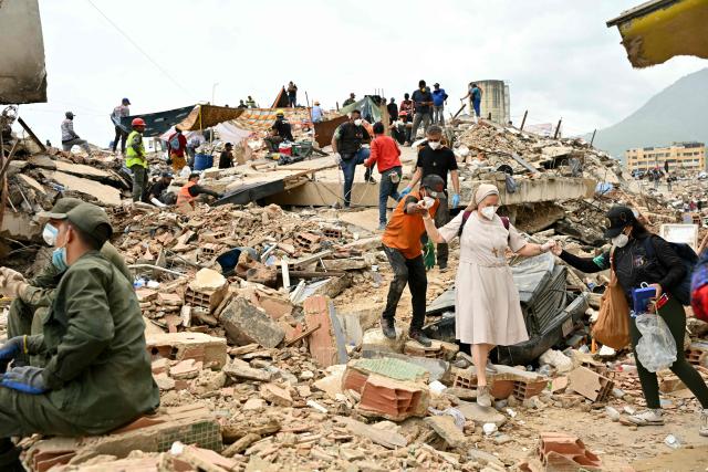 A nun wearing a face mask is assisted across the rubble of collapsed buildings by volunteers in Caraballeda, La Guaira state, Venezuela, on July 3, 2026. The death toll from Venezuela's twin earthquakes has risen to 2,595, Interim President Delcy Rodriguez said on July 2. (Photo by MARTIN BERNETTI / AFP)