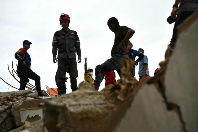 Rescuers stand and move atop the rubble of collapsed buildings as one worker raises an arm in Caraballeda, La Guaira state, Venezuela, on July 3, 2026. The death toll from Venezuela's twin earthquakes has risen to 2,595, Interim President Delcy Rodriguez said on July 2. (Photo by MARTIN BERNETTI / AFP)