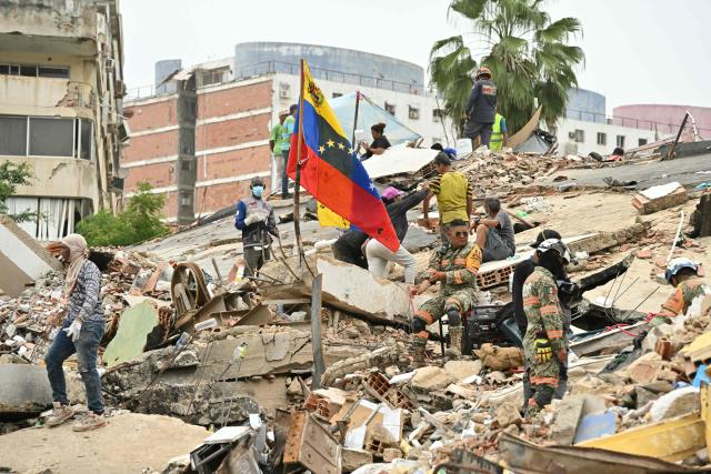 Rescuers and volunteers work amid the rubble of collapsed buildings, as a Venezuelan flag is raised, in Caraballeda, La Guaira state, Venezuela, on July 3, 2026. The death toll from Venezuela's twin earthquakes has risen to 2,595, Interim President Delcy Rodriguez said on July 2. (Photo by MARTIN BERNETTI / AFP)