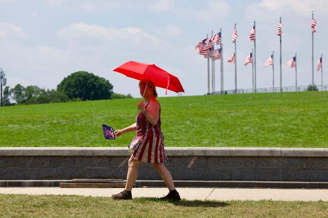 A woman uses an umbrella as people cope with extreme heat along the National Mall in Washington, DC, on July 3, 2026, as high temperatures grip the US capital ahead of Independence Day celebrations. Blistering temperatures and humidity has gripped swaths of the United States this week, with more to come for the densely populated East Coast as the nation co-hosts the World Cup and prepares to celebrate its 250th birthday on July 4. The heat wave that has been broiling the Midwest is intensifying in the Northeast, with temperatures surpassing 100F (38C) in cities including New York, Philadelphia and Washington. (Photo by Amid FARAHI / AFP)