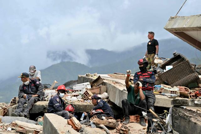 A rescuer raises a clenched fist to signal silence as others halt during search operations amid the rubble of collapsed buildings in Caraballeda, La Guaira state, Venezuela, on July 3, 2026. The death toll from Venezuela's twin earthquakes has risen to 2,595, Interim President Delcy Rodriguez said on July 2. (Photo by MARTIN BERNETTI / AFP)