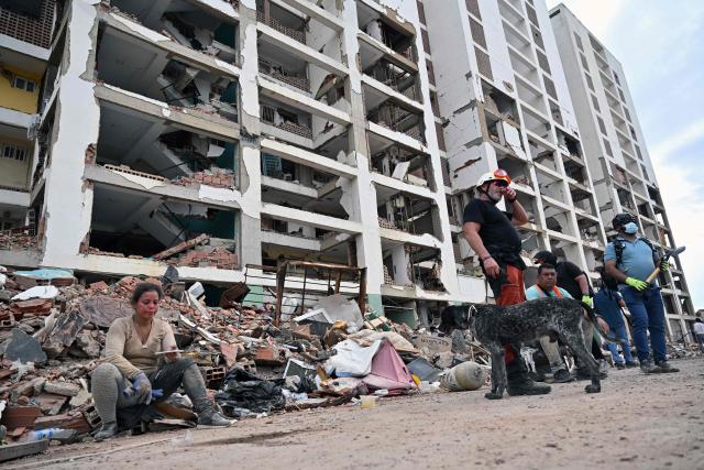 A Spanish rescuer with a search dog rests alongside volunteer rescuers in front of a partially collapsed building in Caraballeda, La Guaira state, Venezuela, on July 3, 2026. The death toll from Venezuela's devastating twin earthquakes has risen to 2,645, with more than 12,600 injured, according to new official figures released on July 3. (Photo by MARTIN BERNETTI / AFP)