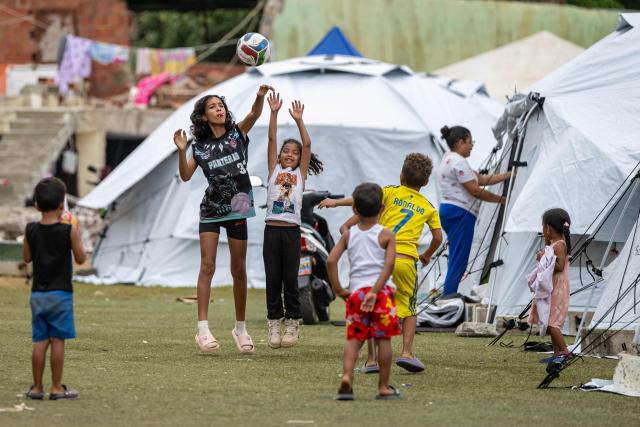 Children play with a ball near tents at the Cesar Nieves baseball stadium in the La Angustia neighborhood of Catia La Mar, La Guaira state, Venezuela, on July 3, 2026, where displaced people have taken refuge. The death toll from Venezuela's devastating twin earthquakes has risen to 2,645, with more than 12,600 injured, according to new official figures released on July 3. (Photo by Miguel MEDINA / AFP)