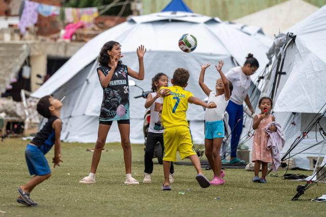 Children play with a ball near tents at the Cesar Nieves baseball stadium in the La Angustia neighborhood of Catia La Mar, La Guaira state, Venezuela, on July 3, 2026, where displaced people have taken refuge. The death toll from Venezuela's devastating twin earthquakes has risen to 2,645, with more than 12,600 injured, according to new official figures released on July 3. (Photo by Miguel MEDINA / AFP)