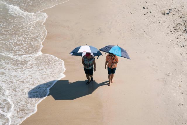 People walk with umbrellas on the beach during a heatwave in Carolina Beach, North Carolina, on July 3, 2026. Blistering temperatures and humidity has gripped swaths of the United States this week, with more to come for the densely populated East Coast as the nation co-hosts the World Cup and prepares to celebrate its 250th birthday on July 4. The heat wave that has been broiling the Midwest is intensifying in the Northeast, with temperatures surpassing 100F (38C) in cities including New York, Philadelphia and Washington. (Photo by Allison Joyce / AFP)