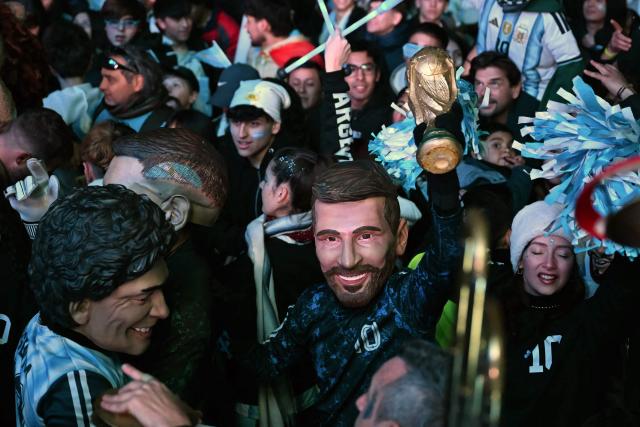 A fan of Argentina wearing a mask of Argentine forward Lionel Messi holds a replica of the FIFA World Cup trophy while watching  the FIFA World Cup 2026 round-of-32 football match between Argentina and Cape Verde on a giant screen, in Buenos Aires on July 3, 2026. (Photo by Luis ROBAYO / AFP)