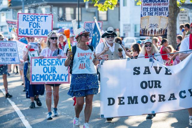 People display political signs as they march during the Gloucester Fishtown Horribles Parade in Gloucester, Massachusetts on July 3, 2026. The parade is part of the city’s July 4th celebrations. (Photo by JOSEPH PREZIOSO / AFP)