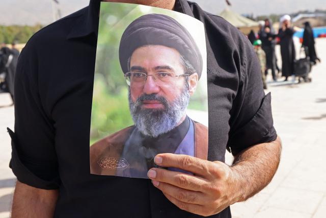 A mourner carries a portrait of Iran's supreme leader Mojtaba Khamenei, upon his arrival at the Grand Mosalla to attend the funeral ceremonies of slain supreme leader Ayatollah Ali Khamenei, in Tehran on July 4, 2026. Funeral ceremonies for Iran's supreme leader Ali Khamenei officially began on July 4, state television reported, an event drawing thousands and intended to serve as a show of strength to the Islamic republic's foes. (Photo by ATTA KENARE / AFP) / 