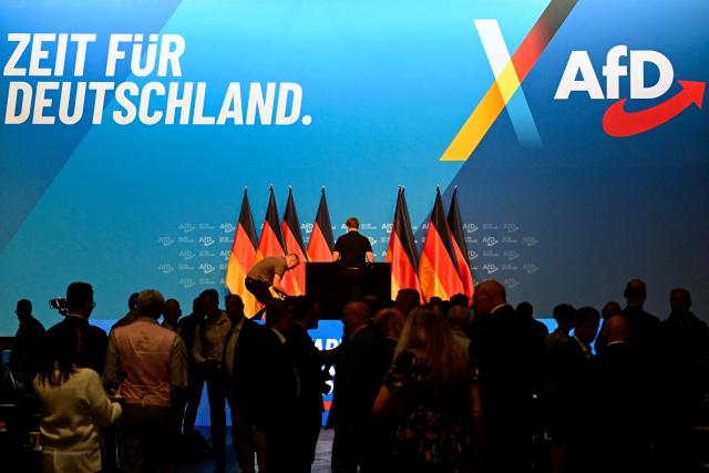 Workers set up the stage and podium with German flags as delegates arrive at the party congress of far-right Alternative for Germany (AfD) at the Messe Erfurt fairground in Erfurt, eastern Germany on early July 4, 2026. German police are bracing to guard an annual congress of the far-right AfD party this weekend (July 4-5) against tens of thousands of antifascist demonstrators who are determined to shut it down. The standoff in the city of Erfurt, Thuringia state, comes as the opposition Alternative for Germany party is soaring in national opinion polls ahead of all other parties. (Photo by John MACDOUGALL / AFP)