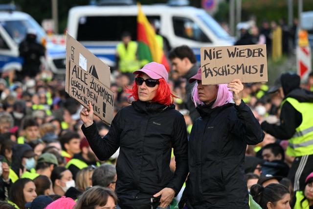Participants hold up placards with the letterings 'All together against fascism' (L) and 'Fascism never again' as demonstrators have gathered for a sit-in to block the access road at Gothaer Platz to the Messe Erfurt fairground in Erfurt, eastern Germany on early July 4, 2026, where the party congress of far-right Alternative for Germany (AfD) will be held from July 4-5. German police are bracing to guard an annual congress of the far-right AfD party this weekend against tens of thousands of antifascist demonstrators who are determined to shut it down. The standoff in the city of Erfurt, Thuringia state, comes as the opposition Alternative for Germany party is soaring in national opinion polls ahead of all other parties. (Photo by RALF HIRSCHBERGER / AFP)