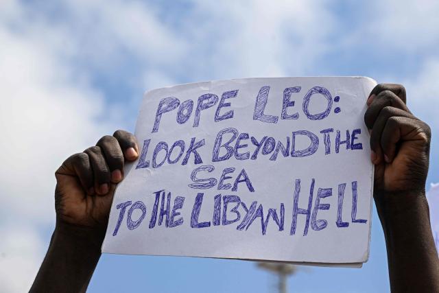A faithful holds a placard reading "Pope Leo look beyond the sea to the Libyan hell" as Pope Leo XIV celebrates the mass during a one day visit to Lampedusa island, south of Sicily, on July 4, 2026. Pope Leo XIV bid Europe on July 4 better its response to the "momentous challenge" of migration, urging it to adopt a strategic approach to integrating new arrivals, as well as improving lives in developing countries. (Photo by Tiziana FABI / AFP)