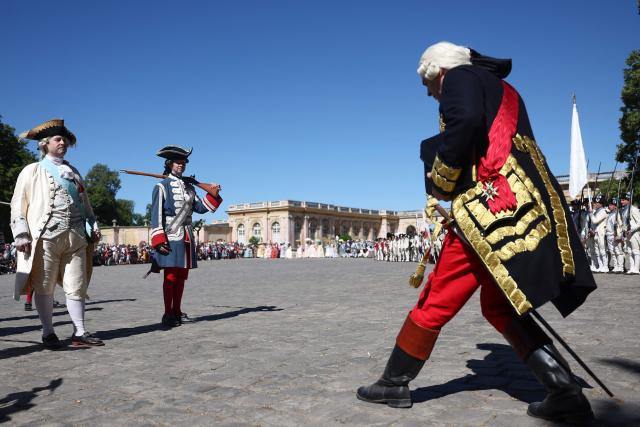 A re-enactor dressed as the king (L) takes part in a historical re-enactment to celebrate the 250th anniversary of the US' Declaration of Independence in the Grand Trianon garden at the Chateau de Versailles, in Versailles in the outskirts of Paris on July 4, 2026. (Photo by ROMAIN PERROCHEAU / AFP)