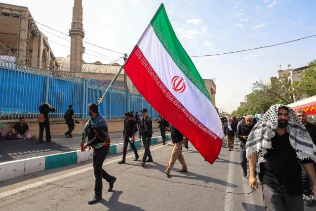 A man waves an Iranian national flag as mourners gather at the Grand Mosalla to pay their final respects to Iran's slain supreme leader Ayatollah Ali Khamenei at the start of his funeral ceremonies in Tehran on July 4, 2026. Funeral ceremonies for Iran's supreme leader Ali Khamenei officially began on July 4, state television reported, an event drawing thousands and intended to serve as a show of strength to the Islamic republic's foes. (Photo by ATTA KENARE / AFP) / 