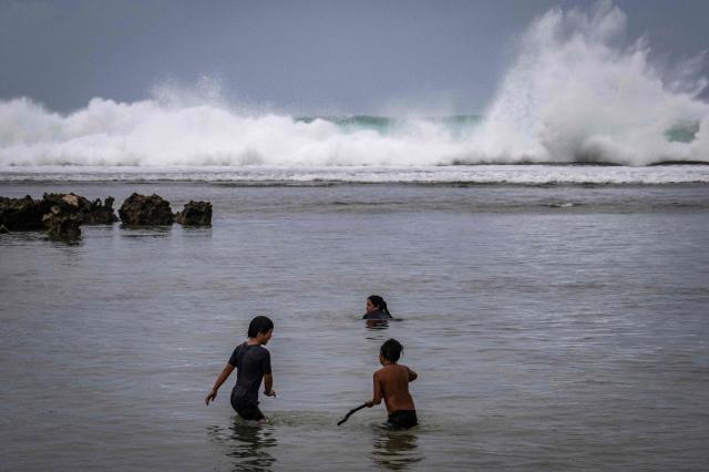 Waves hit the coastline as children play at a beach ahead of the arrival of the forecasted Super Typhoon Bavi in Guam, Northern Mariana Islands, on July 4, 2026. People in Guam and the Northern Marianas readied themselves on July 4 as the second "super typhoon" to threaten the US Pacific territories since April drew closer, bringing the equivalent of category-5 hurricane winds. (Photo by Yuichi YAMAZAKI / AFP)