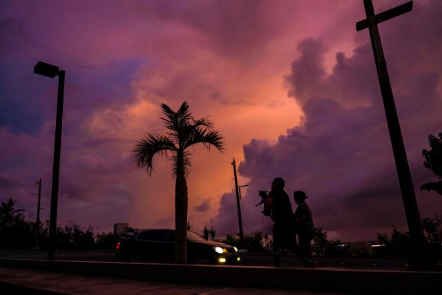 People walk along a street at sunset ahead of the arrival of the forecasted Super Typhoon Bavi in Guam, Northern Mariana Islands, on July 4, 2026. People in Guam and the Northern Marianas readied themselves on July 4 as the second "super typhoon" to threaten the US Pacific territories since April drew closer, bringing the equivalent of category-5 hurricane winds. (Photo by Yuichi YAMAZAKI / AFP)
