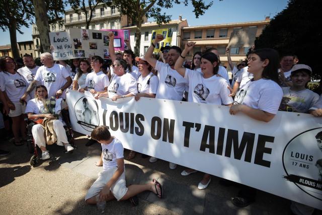 Demonstrators including Louis's father Nicolas Herve (4th R) and his partner (3rd R) hold a banner reading "Louis we love you" as they attend a tribute march to Louis, a teenager killed in an ambush in Narbonne, in Carcassonne, southwestern France, on July 4, 2026. Several hundred people took part on July 4, 2026, afternoon in Carcassonne in a silent march for Louis, a 17-year-old teenager who died at the end of June from injuries sustained in a beating, on the site of a construction project in Narbonne, on the evening of June 19, during an ambush filmed by his attackers. Left unconscious at the scene, he was hospitalized the next day after being discovered by a worker, but died from his injuries on June 23. (Photo by Valentine CHAPUIS / AFP)