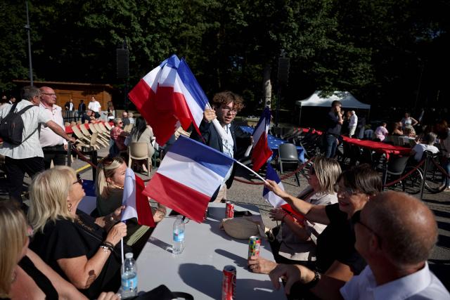 A French far-right party Rassemblement national (RN) activist hands out French flags to participants during a RN party event "La fete champetre" in Lievin, northern France on July 4, 2026. (Photo by SIMON WOHLFAHRT / AFP)