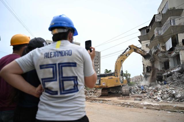 EDITORS NOTE: Graphic content / Relativs of victims watch as a backhoe demolishes a building in La Guaira, Venezuela on July 4, 2026, following the June 24 twin earthquakes. With little hope of finding loved ones alive, frustrated families of those affected by Venezuela's double earthquakes clamor for help to recover their loved one's bodies as uncertainty grows over the death toll from the tragedy. (Photo by Raul ARBOLEDA / AFP)