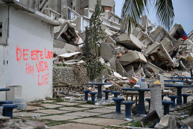 EDITORS NOTE: Graphic content / A wall reads "On this side there is life" next to a destroyed building in La Guaira, Venezuela on July 4, 2026, following the June 24 twin earthquakes. With little hope of finding loved ones alive, frustrated families of those affected by Venezuela's double earthquakes clamor for help to recover their loved one's bodies as uncertainty grows over the death toll from the tragedy. (Photo by Raul ARBOLEDA / AFP)