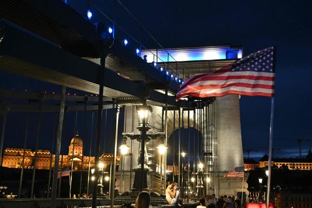 US flags flutter in the breeze as Hungary’s oldest bridge, the Chain Bridge is illuminated in the colors of the United States flag in downtown Budapest on July 4, 2026. The iconic landmark is illuminated in red, white and blue to mark the 250th anniversary of American independence. The special lighting transforms one of Budapest’s most recognizable symbols into a striking tribute spanning the Danube. (Photo by Attila KISBENEDEK / AFP)