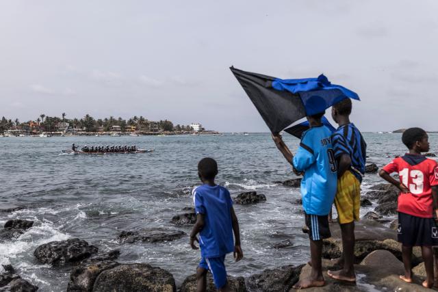 Children wave the flag of the Xataxely community in Ngor village as their pirogue paddles to the starting line during the annual Ngor Regatta, off the coast of Ngor island, in Dakar, on July 4, 2026. Sailors and fishermen from different communities gathered for the annual Ngor Regatta, a sporting event celebrating the culture and traditions of the Lebou people, a traditional fishing community in Senegal. (Photo by PATRICK MEINHARDT / AFP)