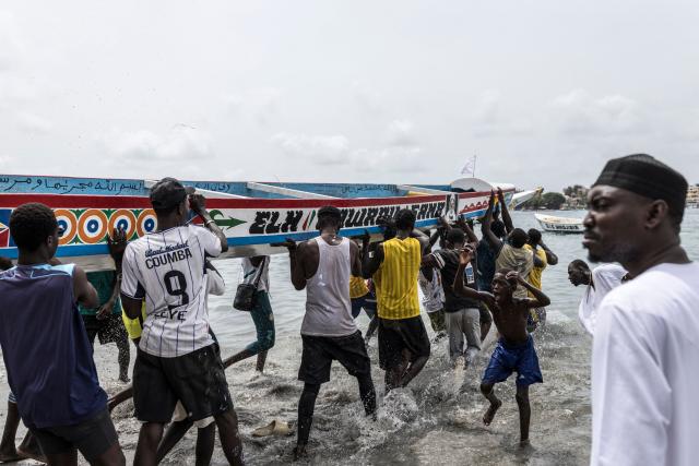 People carry a racing pirogue into the water before the start of the the annual Ngor Regatta, off the coast of Ngor island, in Dakar, on July 4, 2026. Sailors and fishermen from different communities gathered for the annual Ngor Regatta, a sporting event celebrating the culture and traditions of the Lebou people, a traditional fishing community in Senegal. (Photo by PATRICK MEINHARDT / AFP)