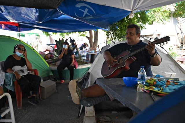 A survivor plays the guitar at a makeshift camp in La Guaira, Venezuela on July 4, 2026, following the June 24 twin earthquakes. With little hope of finding loved ones alive, frustrated families of those affected by Venezuela's double earthquakes clamor for help to recover their loved one's bodies as uncertainty grows over the death toll from the tragedy. (Photo by Raul ARBOLEDA / AFP)