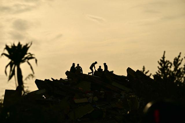 Silhouettes of rescuers stand atop the rubble of a collapsed building in Catia La Mar, La Guaira state, Venezuela on July 4, 2026, following the June 24 twin earthquakes. The death toll from Venezuela's devastating twin earthquakes has risen to 2,954, according to official figures released on Saturday. (Photo by MARTIN BERNETTI / AFP)