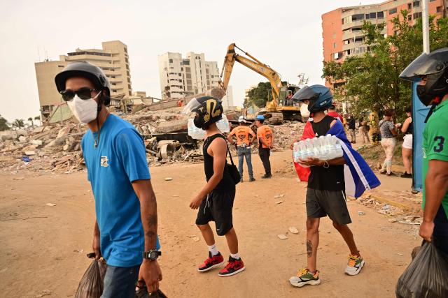Volunteers carry supplies past a collapsed building as rescue workers continue operations in Catia La Mar, La Guaira state, on the outskirts of Caracas, on July 4, 2026, following the June 24 twin earthquakes. The death toll from Venezuela's devastating twin earthquakes has risen to 2,954, according to official figures released on Saturday. (Photo by MARTIN BERNETTI / AFP)