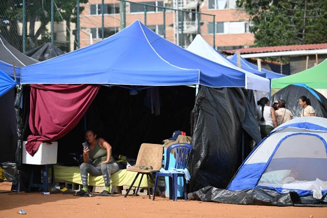 A displaced woman checks her mobile phone inside a tent at a makeshift camp in La Guaira, Venezuela on July 4, 2026, following the June 24 twin earthquakes. With little hope of finding loved ones alive, frustrated families of those affected by Venezuela's double earthquakes clamor for help to recover their loved one's bodies as uncertainty grows over the death toll from the tragedy. (Photo by Raul ARBOLEDA / AFP)