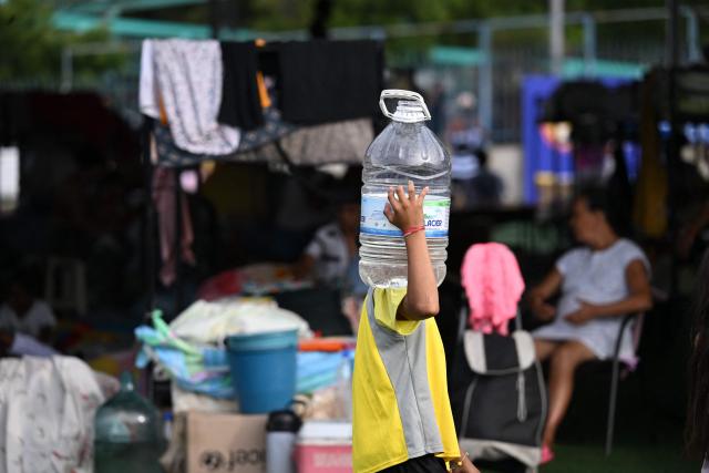 A child holds up a bottle of water near makeshift shelters at the Jose Maria Vargas sports complex in Maiquetia, La Guaira state, Venezuela, on July 3, 2026, following the June 24 twin earthquakes. The death toll from Venezuela's devastating twin earthquakes has risen to 2,954, according to official figures released on Saturday. (Photo by Raul ARBOLEDA / AFP)