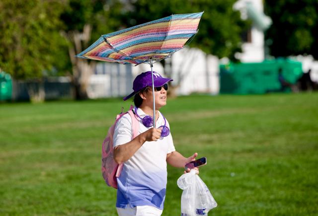 A man attempts to make shade from his broken umbrella as he attends the “Salute to America” Independence Day celebration on the National Mall in Washington, DC, on July 4, 2026. The nation is marking the 250th anniversary of the United States Declaration of Indpendence. (Photo by Amid FARAHI / AFP)