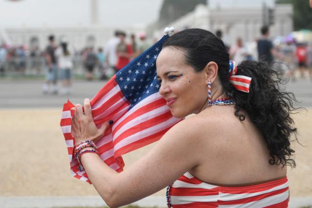 A woman holds small American flags as she attends the Great American State Fair during the "Salute to America" Independence Day celebration on the National Mall in Washington, DC, on July 4, 2026. The nation is marking the 250th anniversary of the United States Declaration of Indpendence. (Photo by Matthew HATCHER / AFP)