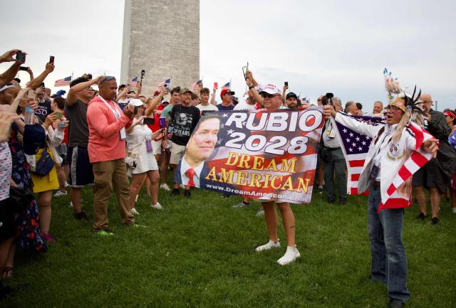 Attendees hold a "Rubio 2028" banner as they gather near the Washington Monument after being evacuated due to thunderstorms during the “Salute to America” Independence Day celebration on the National Mall in Washington, DC, on July 4, 2026. The nation is marking the 250th anniversary of the United States Declaration of Indpendence. (Photo by Amid FARAHI / AFP)