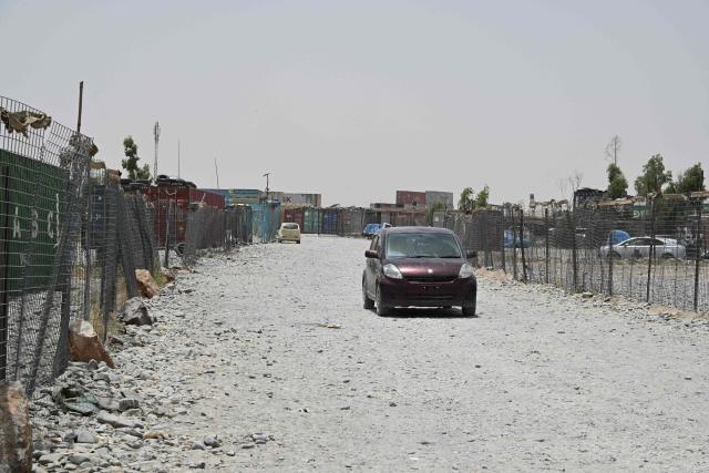 This photograph taken on June 18, 2026 shows a car driving through a vacant container yard in the Spin Boldak district of Afghanistan's Kandahar province. In Afghanistan's southern Kandahar province, a once thriving business of trading car parts from far-flung places has crashed to a halt due to conflicts at the country's borders. (Photo by Sanaullah SEIAM / AFP)