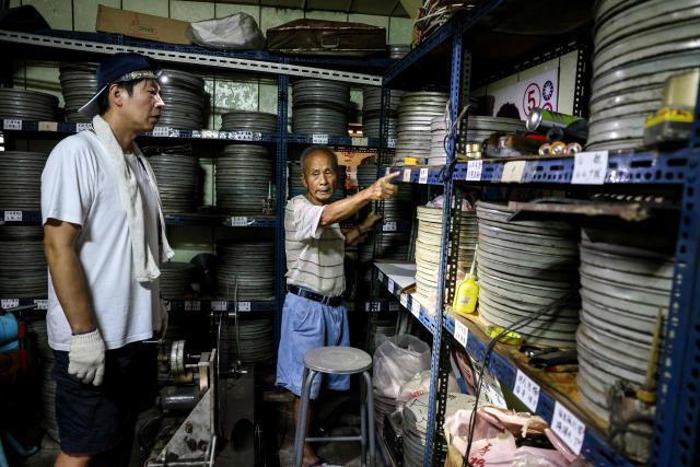Film collector Wang Chin-ting (R) points out to old film reels as he discusses with a staff member from the Taiwan Film and Audiovisual Institute (TFAI) which reels will be collected for restoration and digitisation in Changhua County on May 29, 2026. In a dimly lit red-brick house in central Taiwan, film hunter Wang Wei and his team haul out ageing film reels, salvaging the fragile remnants of a cinema boom that nearly vanished from history. (Photo by I-Hwa Cheng / AFP) / TO GO WITH: Taiwan-culture-history-language, FEATURE by Joy CHIANG