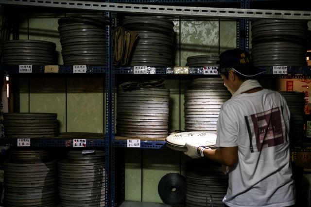 A staff member from the Taiwan Film and Audiovisual Institute selects an old film reel for restoration and digitisation from shelves at a private film archive in Changhua County on May 29, 2026. In a dimly lit red-brick house in central Taiwan, film hunter Wang Wei and his team haul out ageing film reels, salvaging the fragile remnants of a cinema boom that nearly vanished from history. (Photo by I-Hwa Cheng / AFP) / TO GO WITH: Taiwan-culture-history-language, FEATURE by Joy CHIANG