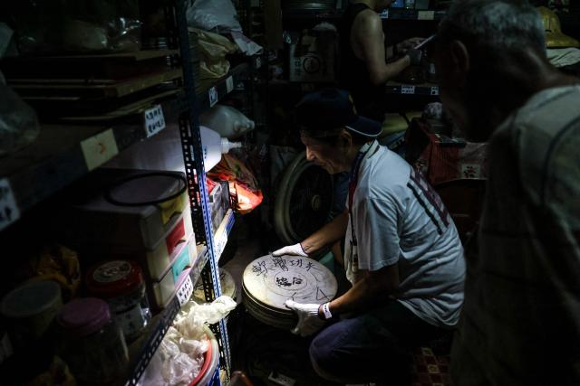 A staff member from the Taiwan Film and Audiovisual Institute retrieves film reels from a cluttered storage room at a private archive in Changhua County on May 29, 2026. In a dimly lit red-brick house in central Taiwan, film hunter Wang Wei and his team haul out ageing film reels, salvaging the fragile remnants of a cinema boom that nearly vanished from history. (Photo by I-Hwa Cheng / AFP) / TO GO WITH: Taiwan-culture-history-language, FEATURE by Joy CHIANG