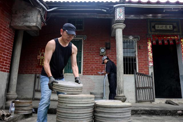 A staff member from the Taiwan Film and Audiovisual Institute stacks dozens of old film reels outside a private archive before they are transported for restoration and digitisation in Changhua County on May 29, 2026. In a dimly lit red-brick house in central Taiwan, film hunter Wang Wei and his team haul out ageing film reels, salvaging the fragile remnants of a cinema boom that nearly vanished from history. (Photo by I-Hwa Cheng / AFP) / TO GO WITH: Taiwan-culture-history-language, FEATURE by Joy CHIANG