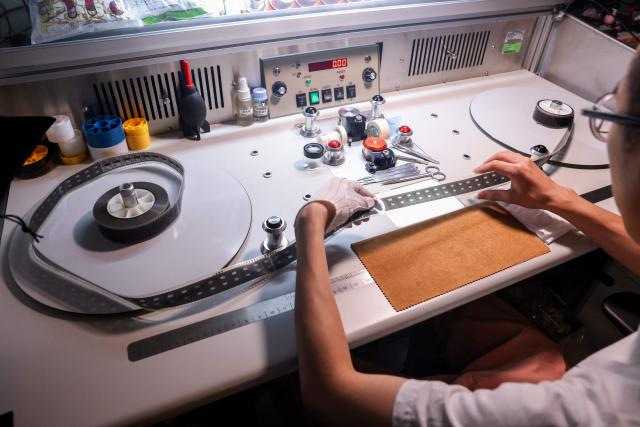 A technician at Preservation and Restoration Center inspects frames of an old film at the Taiwan Film and Audiovisual Institute in New Taipei City on June 23, 2026. In a dimly lit red-brick house in central Taiwan, film hunter Wang Wei and his team haul out ageing film reels, salvaging the fragile remnants of a cinema boom that nearly vanished from history. (Photo by I-Hwa Cheng / AFP) / TO GO WITH: Taiwan-culture-history-language, FEATURE by Joy CHIANG