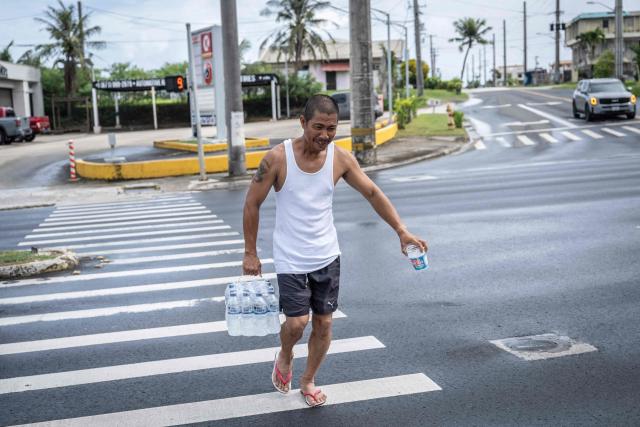 A man carrying supplies crosses a street as the forecasted Super Typhoon Bavi approaches in Guam, Northern Mariana Islands, on July 5, 2026. (Photo by Yuichi YAMAZAKI / AFP)