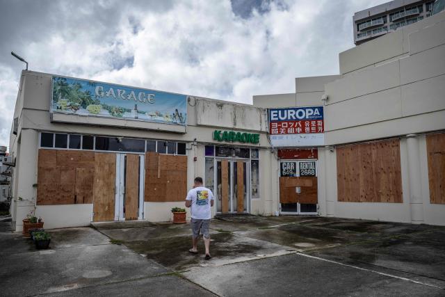A man walks past stores boarded up with plywood as the forecasted Super Typhoon Bavi approaches in Guam, Northern Mariana Islands, on July 5, 2026. (Photo by Yuichi YAMAZAKI / AFP)