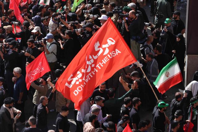 A mourner carries a flag displaying the words "Down With The USA" as they gather to pray for Iran's slain supreme leader Ayatollah Ali Khamenei during the second day of funeral ceremonies at the Grand Mosalla in Tehran on July 5, 2026. Prayers were held July 5 over the casket of Iran's late supreme leader Ali Khamenei, the second day of funeral ceremonies that have drawn huge crowds to pay their final respects in Tehran. Khamenei ruled the Islamic republic from 1989 until he was killed aged 86 in an airstrike on the first day of the US-Israeli war with Iran on February 28. (Photo by ATTA KENARE / AFP) / 