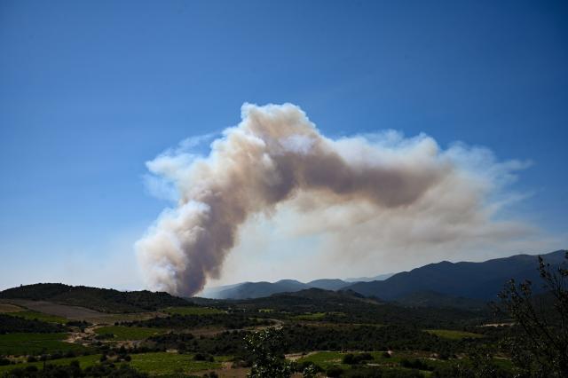This photograph shows smoke rising from a wildfire, near Trevillach, southern France, on July 5, 2026. A wildfire broke out on July 4 at around 19h30 (1730 GMT) in a hard-to-reach massif near Trevillach, in the Pyrenees-Orientales department of southern France and spread rapidly overnight, burning through nearly 1,000 hectares by the morning of July 5, but the fire is no longer spreading freely, according to the prefecture. More than 580 firefighters have been deployed on the ground to fight the blaze. (Photo by Matthieu RONDEL / AFP)