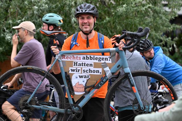 A participant of a bicycle rally shows his bike while wearing a placard with the lettering reading 'Turning right ? - We've had that' in Erfurt, eastern Germany on July 5, 2026, on the second day of a party congress of far-right Alternative for Germany (AfD). Tens of thousands of demonstrators flooded the German city of Erfurt on July 4, blocking major roads and disrupting public transport, but failed to halt a congress of the far-right AfD party. (Photo by RALF HIRSCHBERGER / AFP)