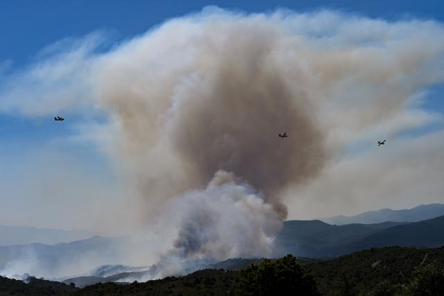 Canadair CL-415 aircrafts of France's Civil Security services fly over smoke rising from a wildfire at the Col des Auzines, near Trevillach, southern France, on July 5, 2026. A wildfire broke out on July 4 at around 19h30 (1730 GMT) in a hard-to-reach massif near Trevillach, in the Pyrenees-Orientales department of southern France and spread rapidly overnight, burning through nearly 1,000 hectares by the morning of July 5, but the fire is no longer spreading freely, according to the prefecture. More than 580 firefighters have been deployed on the ground to fight the blaze. (Photo by Matthieu RONDEL / AFP)
