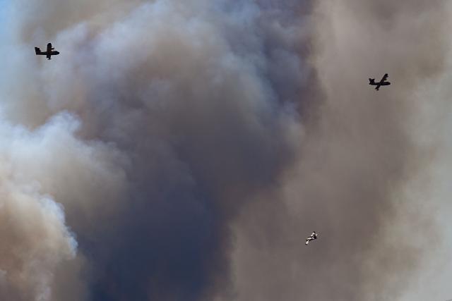 Canadair CL-415 aircrafts of France's Civil Security services fly over smoke rising from a wildfire at the Col des Auzines, near Trevillach, southern France, on July 5, 2026. A wildfire broke out on July 4 at around 19h30 (1730 GMT) in a hard-to-reach massif near Trevillach, in the Pyrenees-Orientales department of southern France and spread rapidly overnight, burning through nearly 1,000 hectares by the morning of July 5, but the fire is no longer spreading freely, according to the prefecture. More than 580 firefighters have been deployed on the ground to fight the blaze. (Photo by Matthieu RONDEL / AFP)