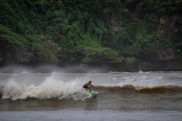 A surfer rides a high wave due to the effects of Super Typhoon Bavi in Guam on July 5, 2026. People in Guam and the Northern Marianas moved to emergency evacuation centers and made last-minute preparations on July 5, hours before a "super typhoon" was projected to bulldoze through the US Pacific territories. (Photo by Yuichi YAMAZAKI / AFP)